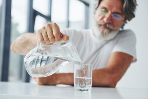 "גבר מבוגר מוזג לעצמו מים מקנקן - המחשה של הפחתת צריכת קפאין והפחתת מים לאחר ניתוח ערמונית"